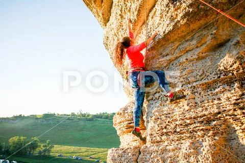 Picture of curly-haired female tourist clambering over rock Stock Photos