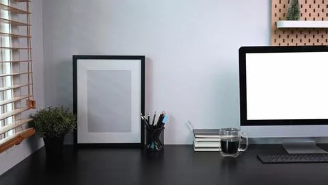 Picture frame, computer with blank screen and houseplant on black table. Stock Photos