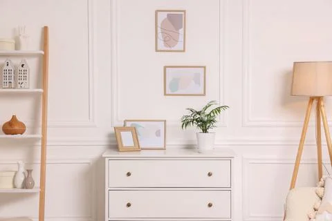 Picture frames hanging on white wall and chest of drawers at home Stock Photos