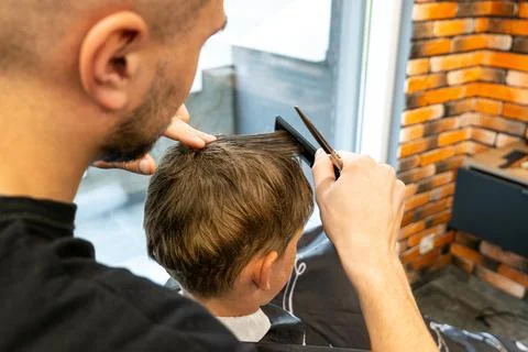 The picture of a small child while sitting on the barbershop chair and being Stock Photos
