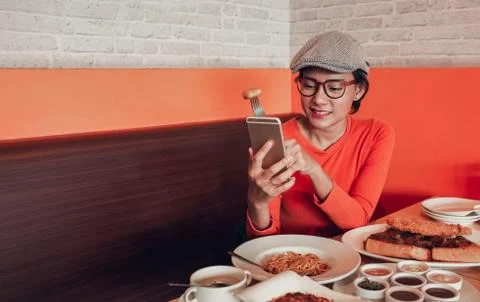 Pictures of Asian women who are eating and using her mobile phone at the same Stock Photos
