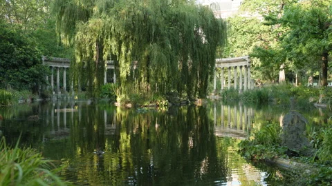 Picturesque View of Ancient Columns Reflecting in a Tranquil Park Pond Framed by Stock Footage 340477450
