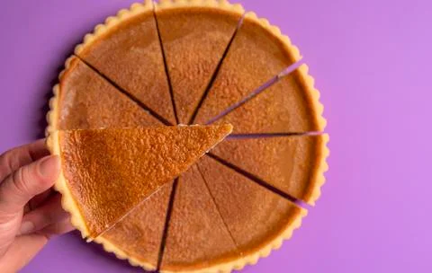 Pie slice held in hand over a whole pumpkin pie. Above view. Stock Photos