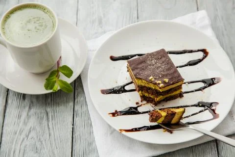 Piece of Austrian three-layer cake and cup of matcha tea on a white plate in Stock Photos