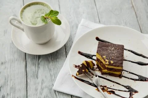 Piece of Austrian three-layer cake and cup of matcha tea on a white plate in Stock Photos