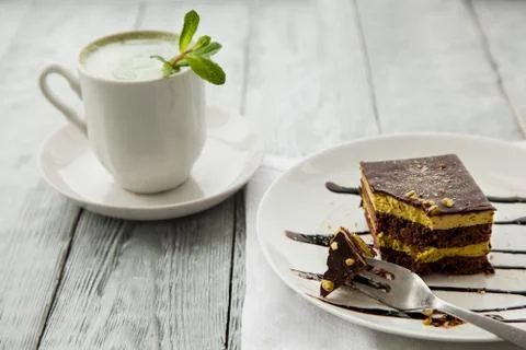 Piece of Austrian three-layer cake and cup of matcha tea on a white plate in Foto stock
