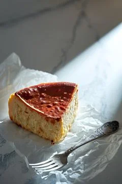 A piece of Basque cheesecake on parchment with a fork. Sunlight in the morn.. Foto stock