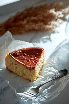A piece of Basque cheesecake on parchment with a fork. Sunlight in the morn.. Stock Photos
