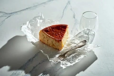 A piece of Basque cheesecake on parchment with a fork. Sunlight in the morn.. Stock Photos