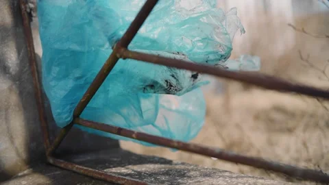 A piece of blue plastic wrap hangs from a metal fence and moves in the wind 스톡 동영상 153231258