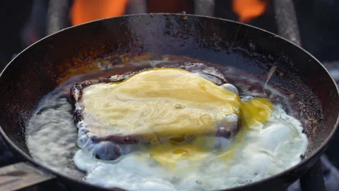 Piece bread and egg is fried in frying pan outdoors with sizzling oil and smoke Stock Footage 260334100