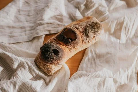 A piece of bread with burnt edges sits on a white cloth 스톡 사진