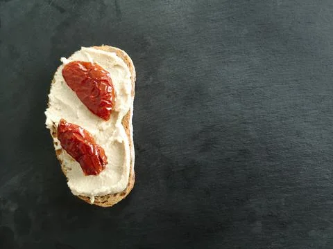 A piece of bread with soft cheese and jerky is on half a table of dark grey m Stock Photos