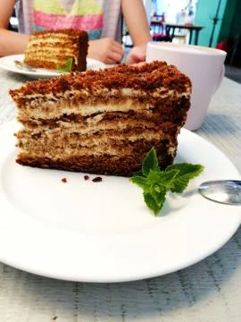 A piece of brown cake with mint leaf on a white plate on a table in a cafe Stock Photos