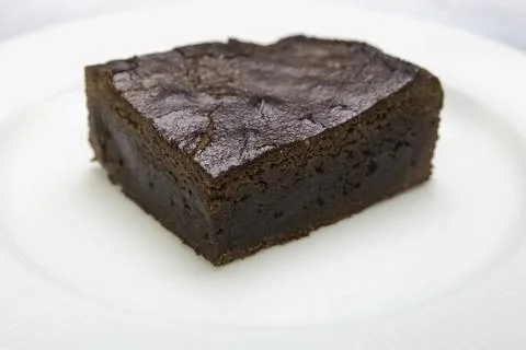 A piece of brown sponge cake on a white plate on table Stock Photos