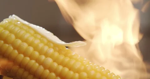 Piece of butter melts on hot corn with blazing fire in the background Stock Footage 124070635