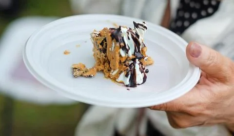 A piece of cake on a plastic plate in hand. Meringue cake with walnuts Stock Photos