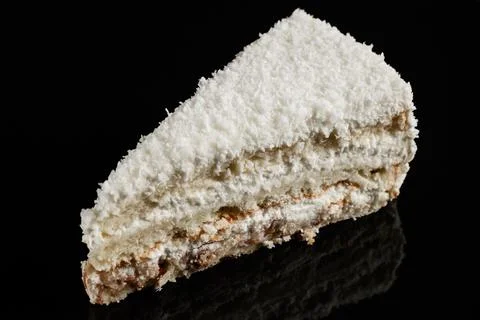 Piece of cake with white coconut chips on a black mirror background. Photos