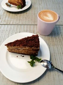 A piece of cake on a white plate on a table in a cafe near a cup of coffee ca Stock Photos
