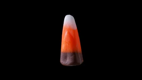 A piece of candy corn is seen floating and rotating. It is seen zooming in Stock Footage 116399811