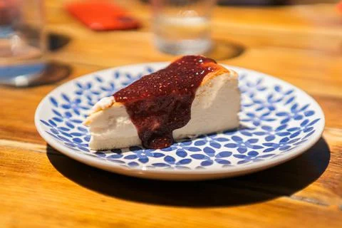 Piece of cheesecake with raspberry jam on top served on a blue-patterned plate o Stock Photos