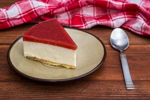 Piece of cheesecake with raspberry jelly on ceramic plate with tea spoon on w Stock Photos