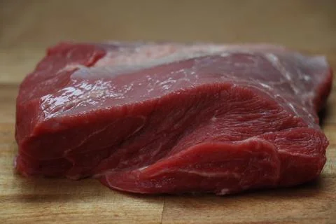 Piece of cut red meat with visible fat on a wooden kitchen chopping board Stock Photos