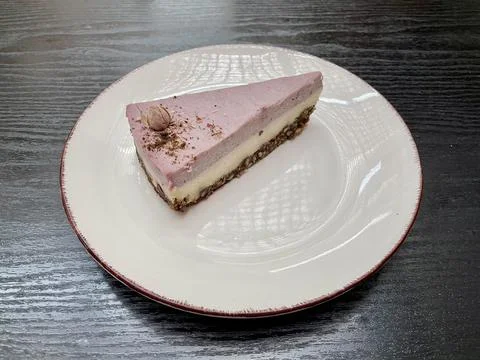 A piece of delicious raspberry raw cheesecake on a white plate lying on a black Foto stock