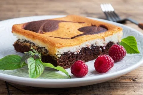 A piece of double-layer cake on a plate of chocolate brownies and curd chee.. 스톡 사진