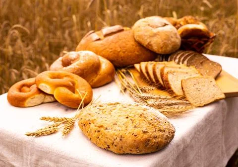 Piece of fresh bread on table against background of grain field Stock Photos