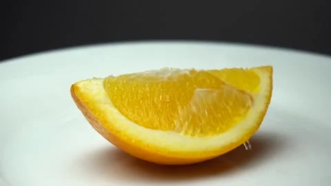 A piece of fresh orange fruit is rotating on the white plate with water drops. Stock Footage 85744297