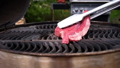 A piece of fresh red meat is put on a hot grill with tongs Stock Footage 157660077