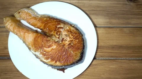 Piece of fried red fish on a plate on a wooden table close-up Stock Footage 85084675