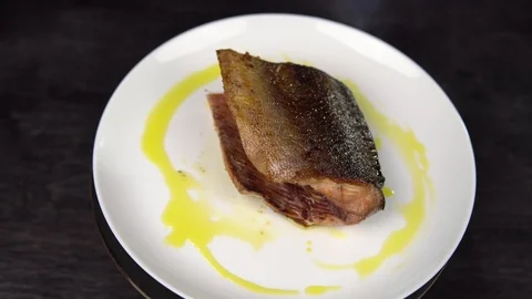 Piece of fried red fish on white plate rotates against black table. Stock Footage 111818887