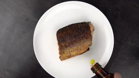 Piece of fried red fish on white plate rotates against black table. Stock Footage 111819064