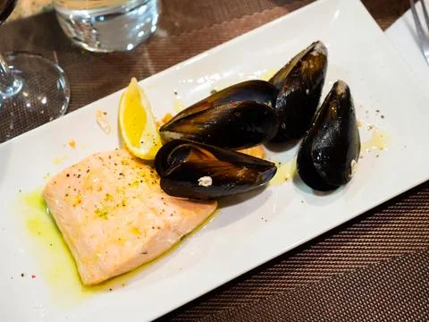 Piece of fried salmon is served on rectangular plate, and decorated with mussels 스톡 사진
