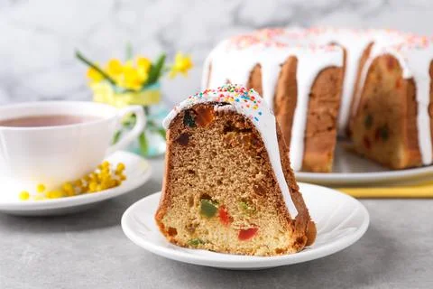 Piece of glazed Easter cake with sprinkles and candied fruits on grey table,  Stock Photos