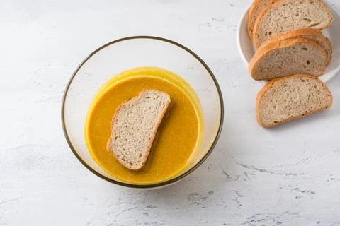 A piece of grain bread is dipped into a spiced, pumpkin mixture on a light blue Stock Photos