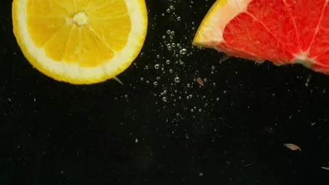 A piece of grapefruit and an orange fall into the water on a black background. Stock Footage 261852915