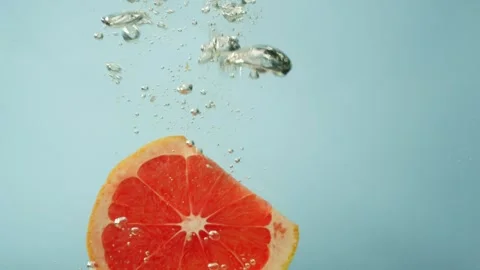 A piece of grapefruit falls into the water creating large bubbles. Stock Footage 256645060