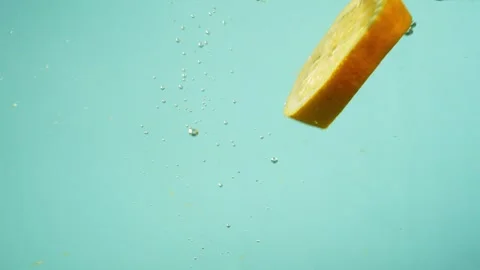 A piece of grapefruit falls into the water, creating air bubbles. Video stock 265848928