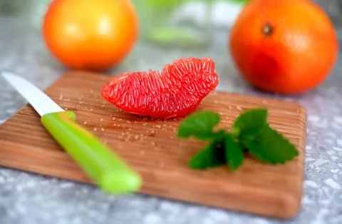 Piece of grapefruit, mint leaf and knife on cutting board. Stock Photos