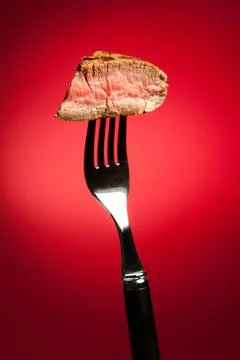 Piece of a grilled steak on a fork isolated on red Stock Photos