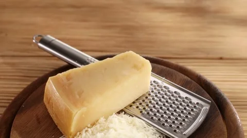 A piece of hard cheese and grated cheese with a grater on a cutting board Stock Footage 244449555