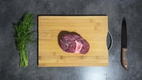 Piece of meat on bone falls from above on wooden cutting board Video stock 295574080