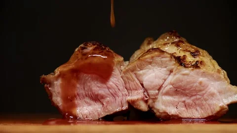 Piece of medium-rare pork steak cut into two parts is poured on top with an Stock Footage 156655016