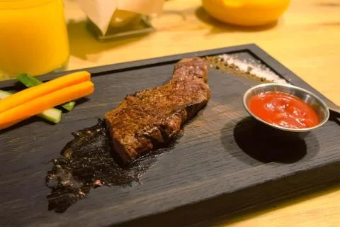 Piece of medium-roasted beef served on a black wooden Board in cafe. Stock Photos