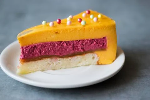A piece of mousse cake with a taste of mango and strawberry on a white plate. Stock Photos