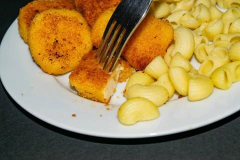 A piece of nuggets on a fork and a white plate with fried chicken nuggets, pa Stock Photos