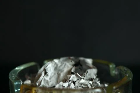 A piece of paper burning down in a glass ashtray close up Stock Photos